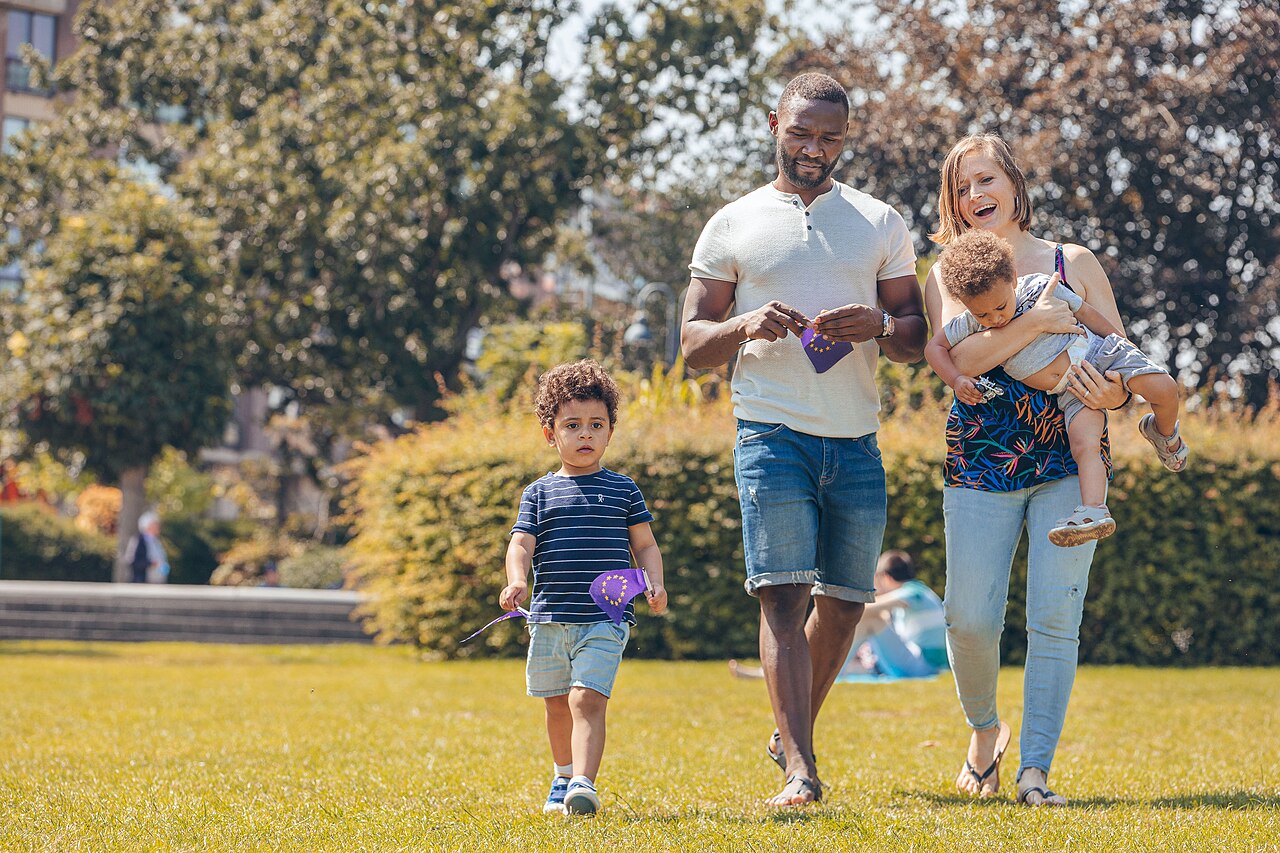 Eine Familie mit zwei kleinen Kindern geht über eine Wiese im Park.